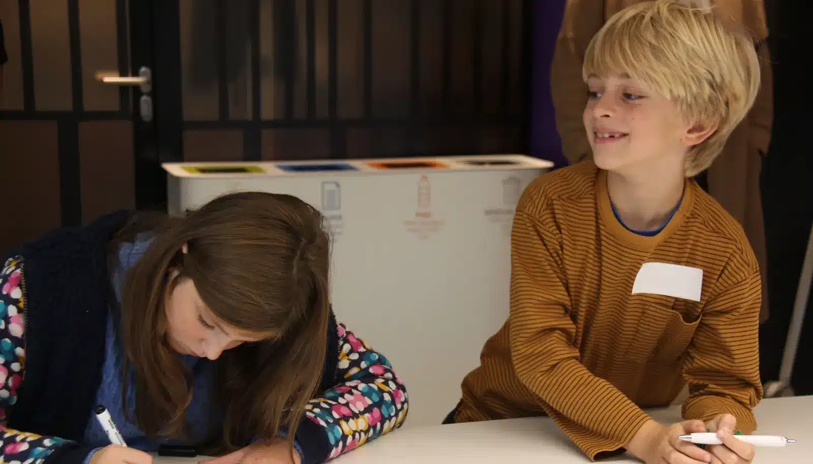 Vier kinderen op een rij aan een tafel, kijken naar een leraar